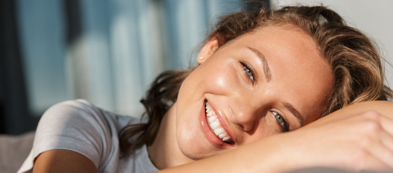 Mladá žena se zářivým úsměvem pohodlně leží s rukou podepřenou hlavou.